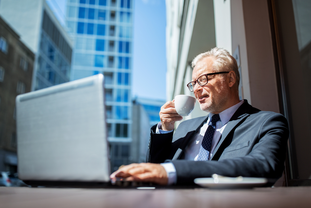 senior businessman with laptop computer drinking coffee at city street